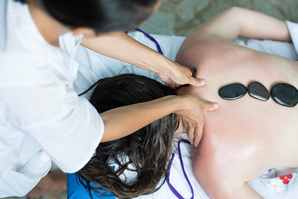 mulher sendo massageda com o auxílio de pedras quentes

